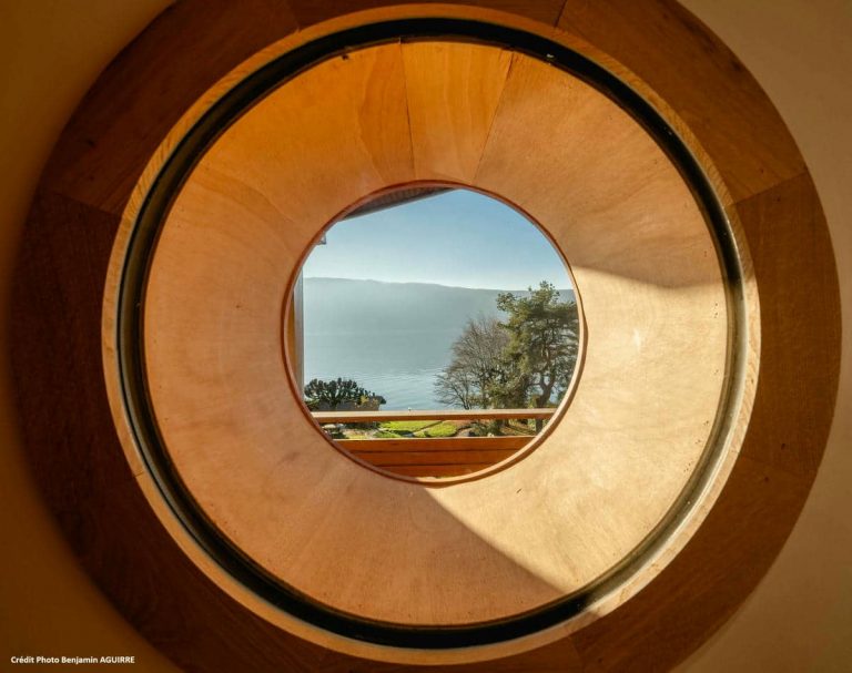 Fenêtre ronde en bois cadrant la vue sur le lac d’Annecy
